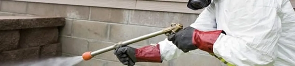 Pest control technician applying exterior insect treatment along a home foundation in Austin, TX