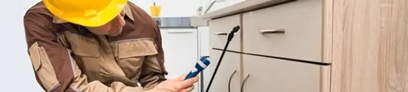 Roach exterminator applying treatment under kitchen cabinets in Austin, TX