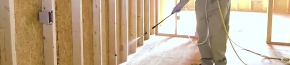Termite treatment technician applying spray along framing and unfinished walls in Austin, TX