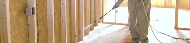Termite treatment technician applying spray along framing and unfinished walls in Austin, TX